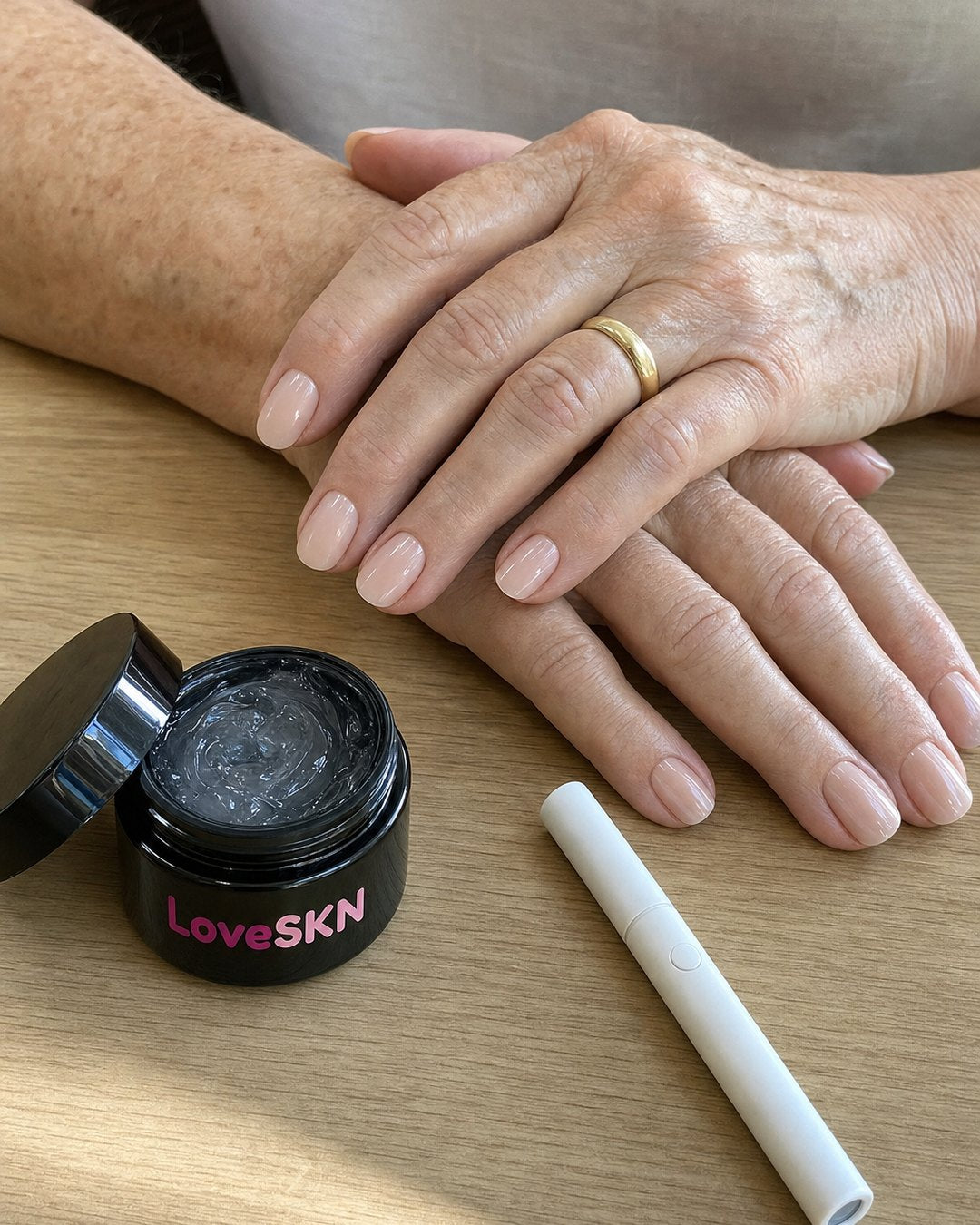 Short milky nude LoveSKN press-on nails on a woman's hands, with the jelly glue jar and the pink UV wand
